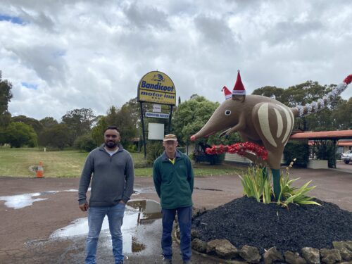 Two men standing out the front of a motor inn with a giant bandicoot sculpture next to them